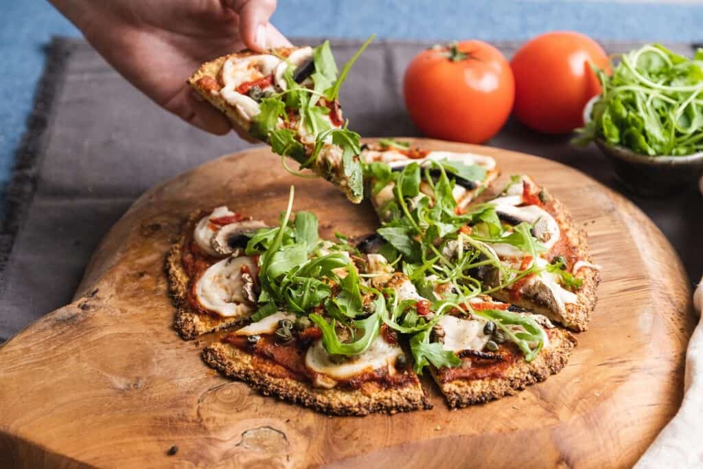Hand grabbing a slice of this dairy free cauliflower pizza crust with vegetarian toppings 