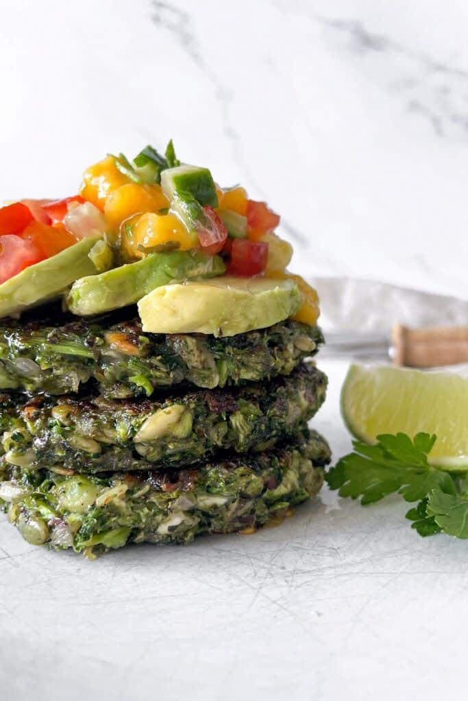 vegan broccoli fritters stacked with mango salsa and avocado on top
