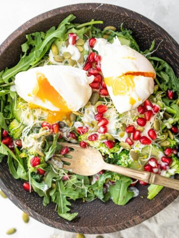 Rocket salad with poached eggs with runny yolk and fork on plate