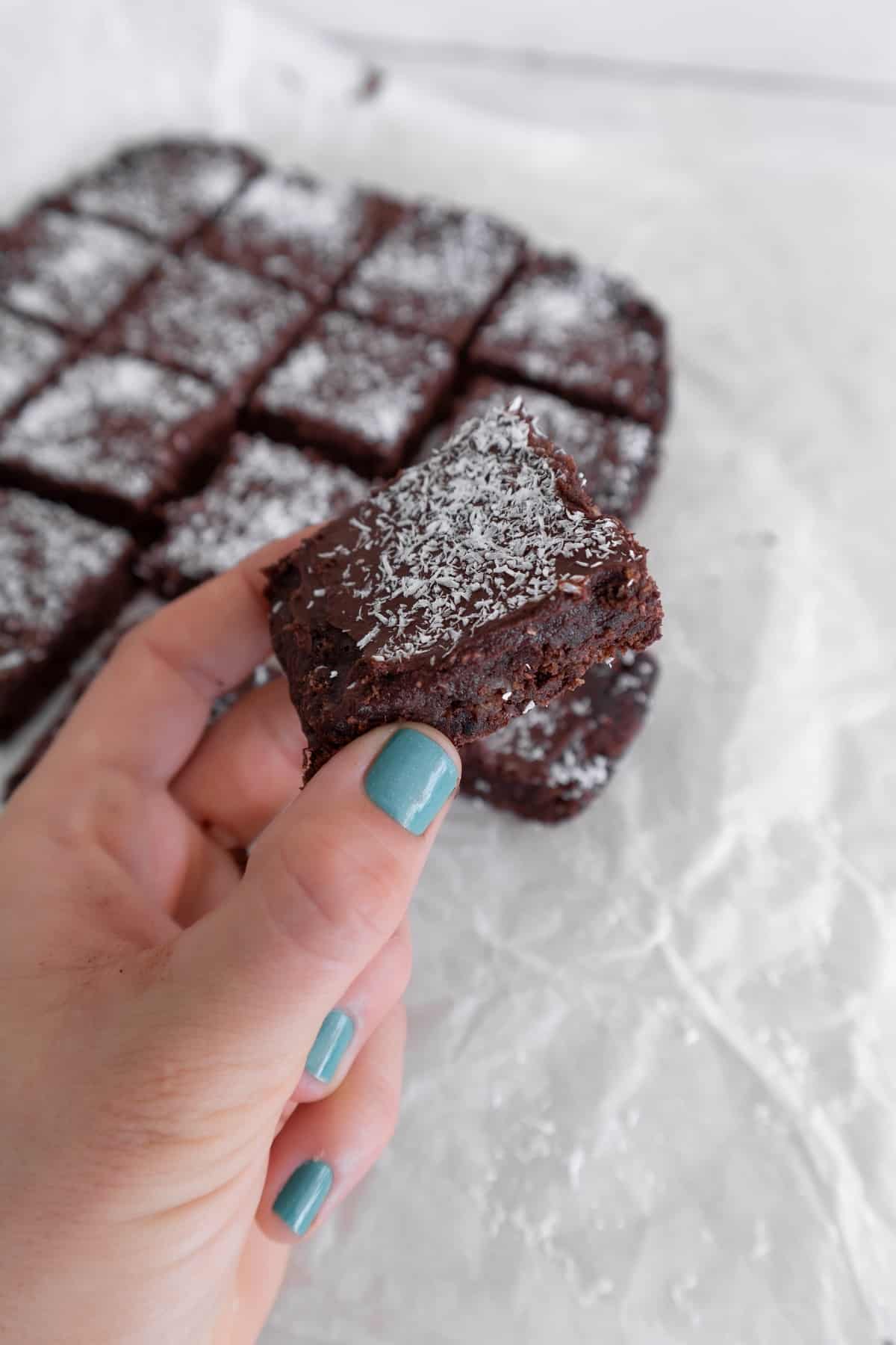 Hand grabbing one square of chocolate coconut slice