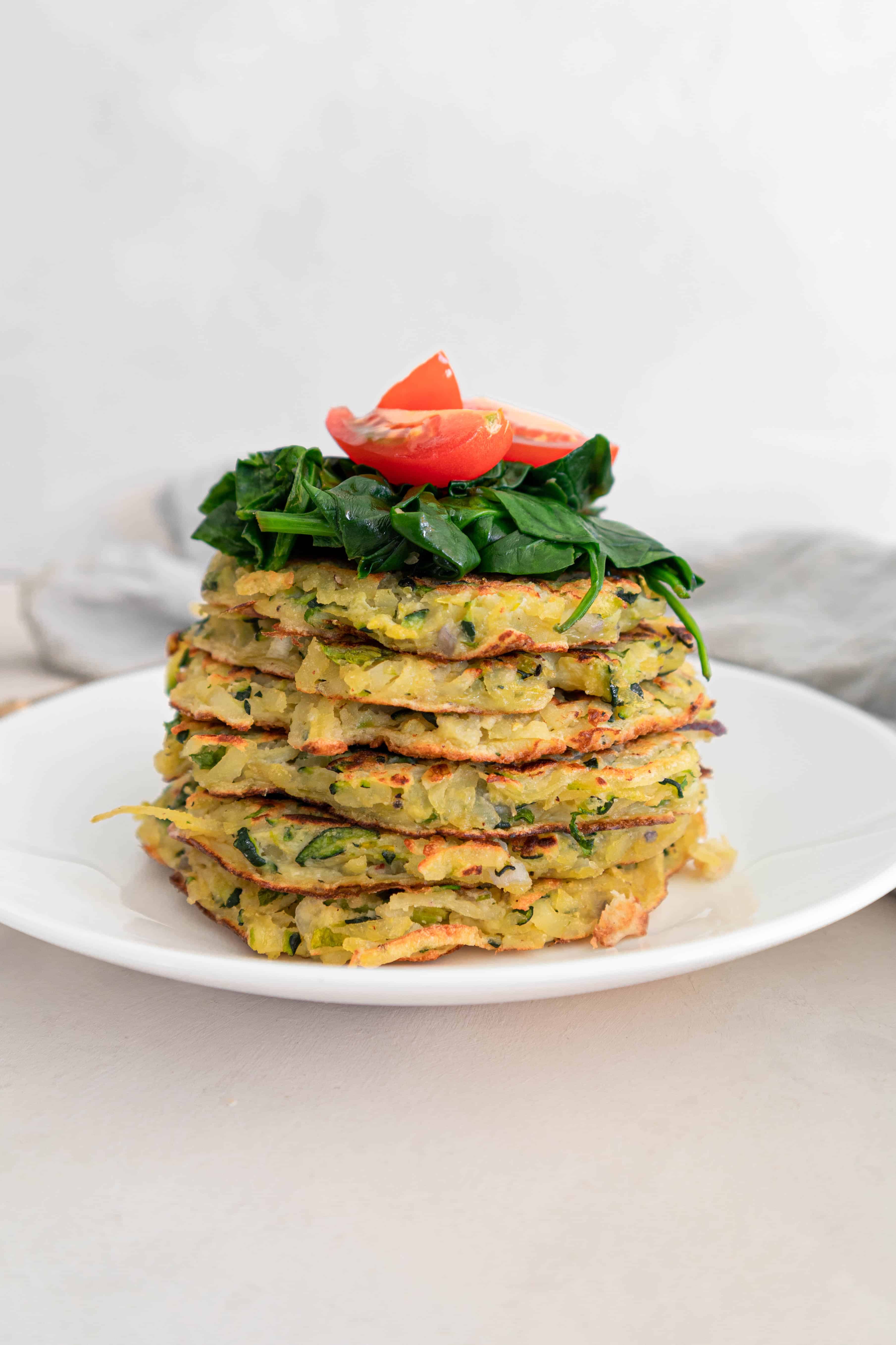 Stack of zucchini and potato fritters (Gluten-free) with wilted spinach and tomato