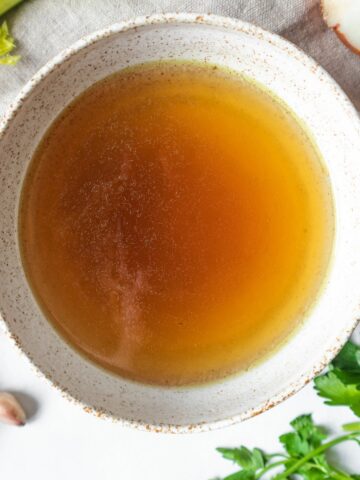 Healing chicken bone broth in a bowl, with veggies around