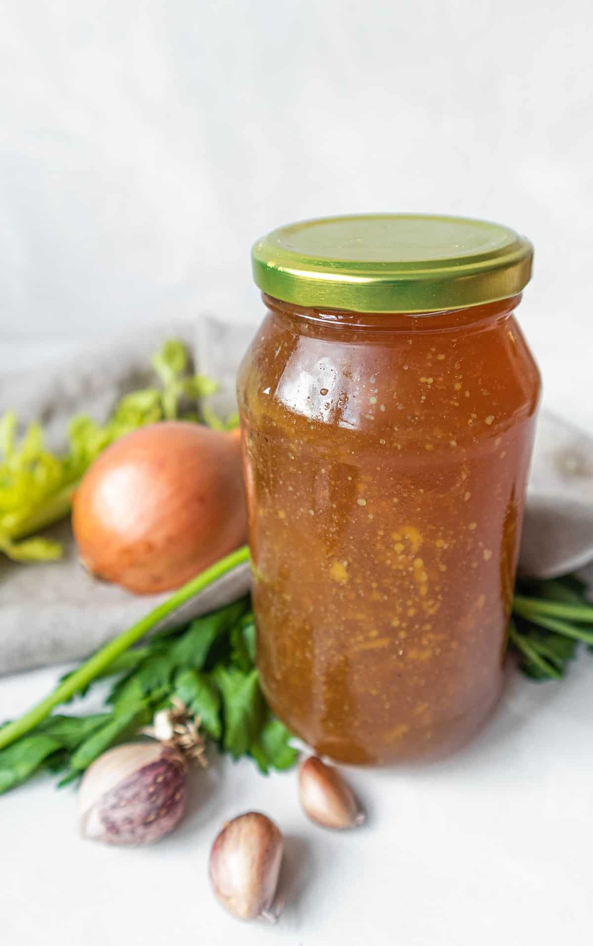 Healing chicken bone broth in a glass jar, with veggies around