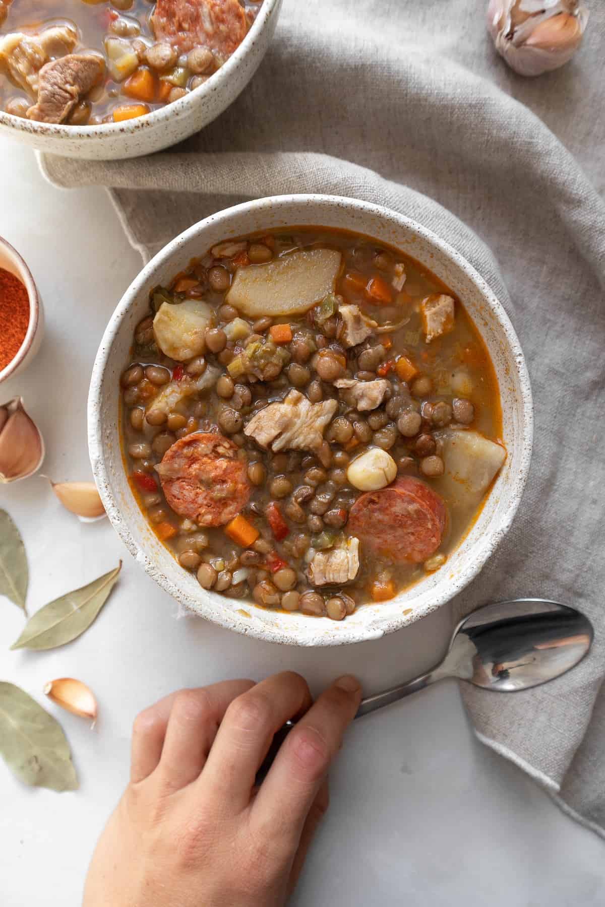 Bowl of Spanish lentil stew and hand grabbing spoon