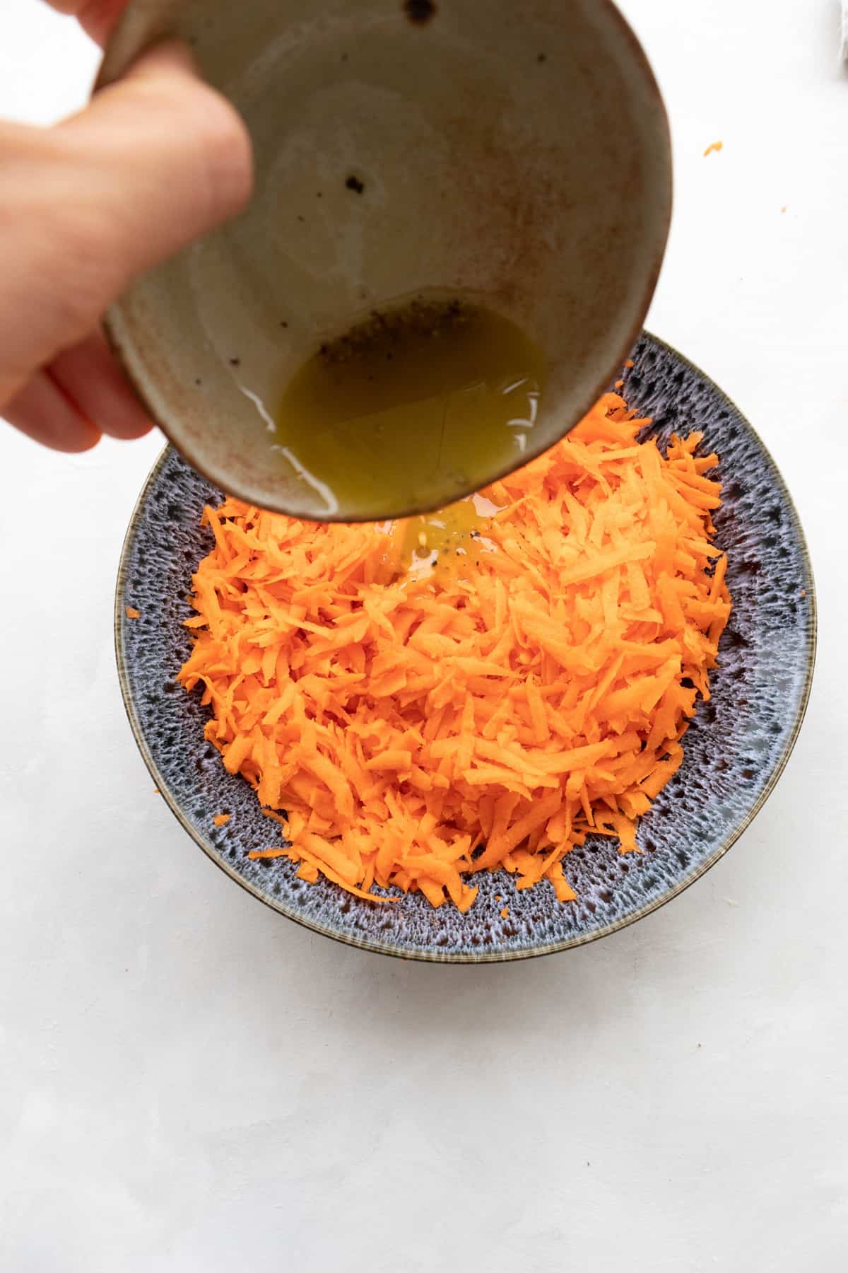 hand pouring the lemon dressing over shredded carrots
