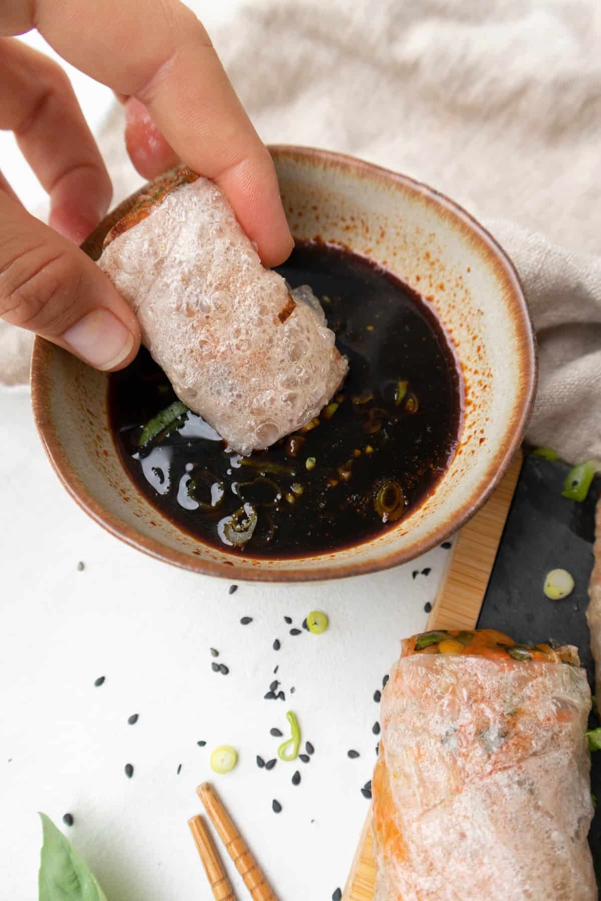 Hand dipping crispy air fryer rice paper roll in sauce