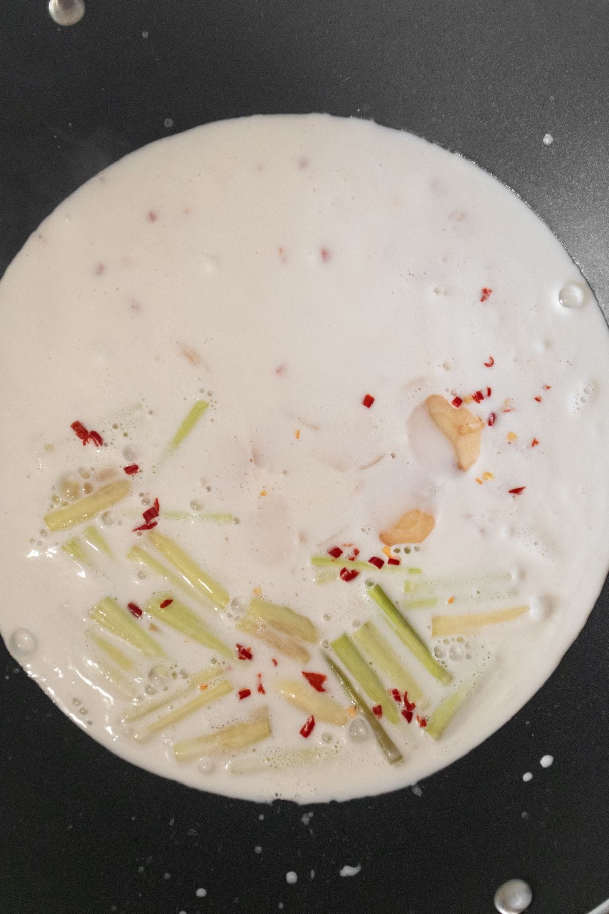 Coconut chicken broth cooking with aromatics on a wok